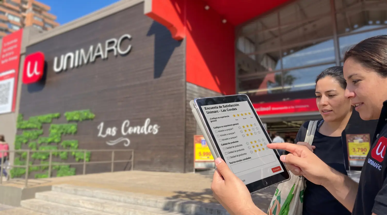 Dos personas revisando una encuesta en una tablet frente a un local de Unimarc